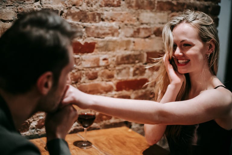 dating standards - Unrecognizable young man kissing hand of young cheerful blond woman sitting at table in cafe